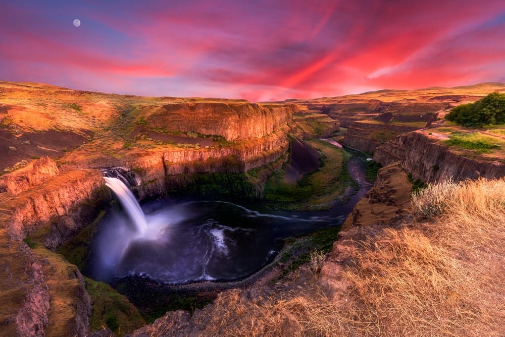 Palouse Falls dropping into a deep canyon at sunset under a dramatic pink sky in eastern Washington.