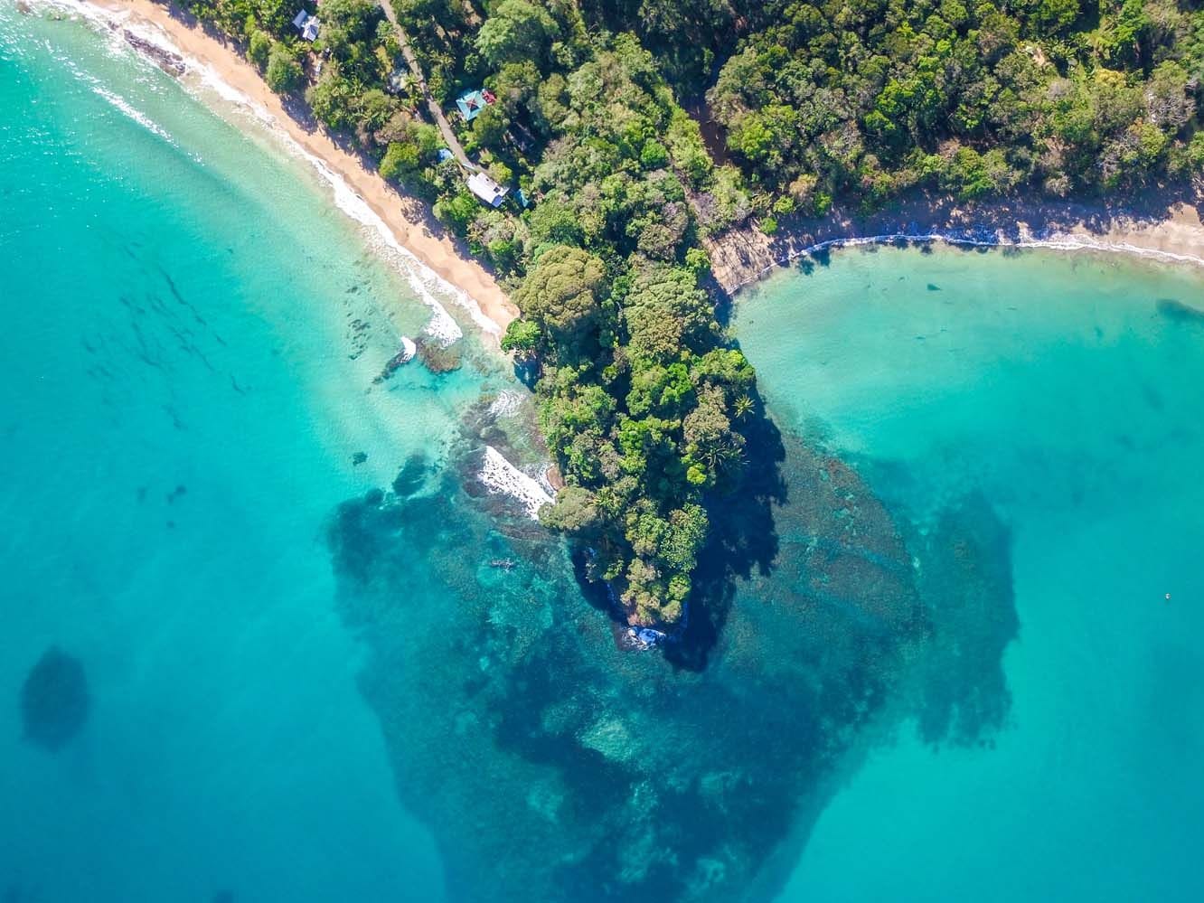 Overhead view of Punta Uva beach in Costa Rica, where lush green jungle meets clear turquoise waters and coral reefs in a tranquil coastal inlet.
