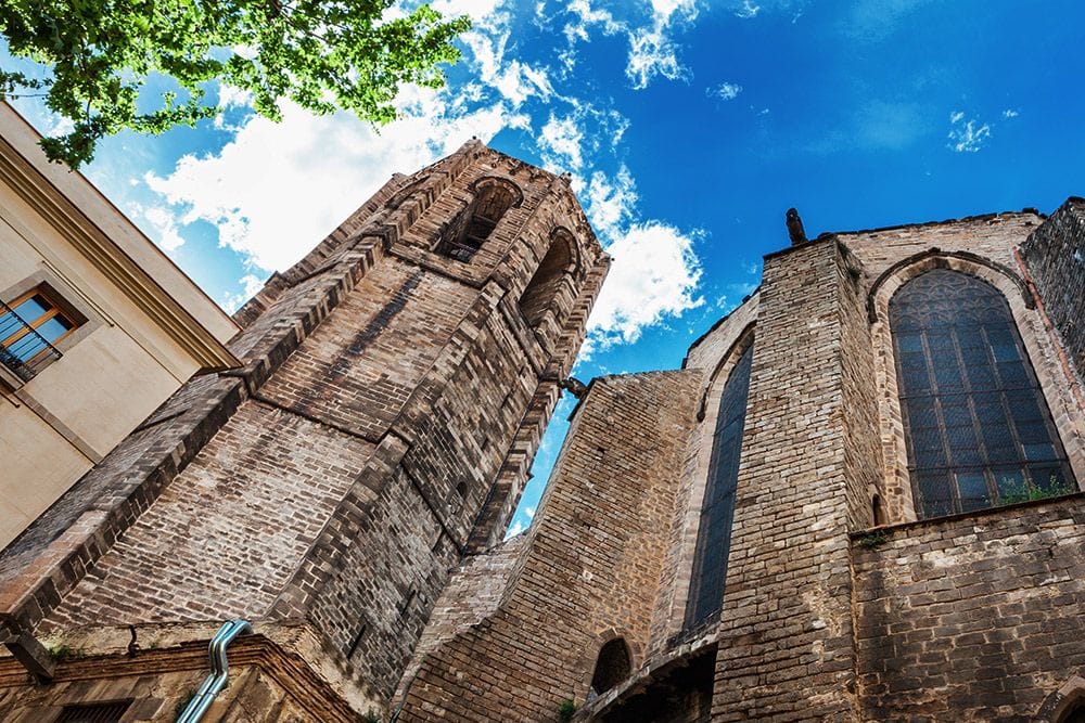 Bell tower of Santa Maria del Pi, Barcelona, Gothic stone walls, arched windows, blue sky.