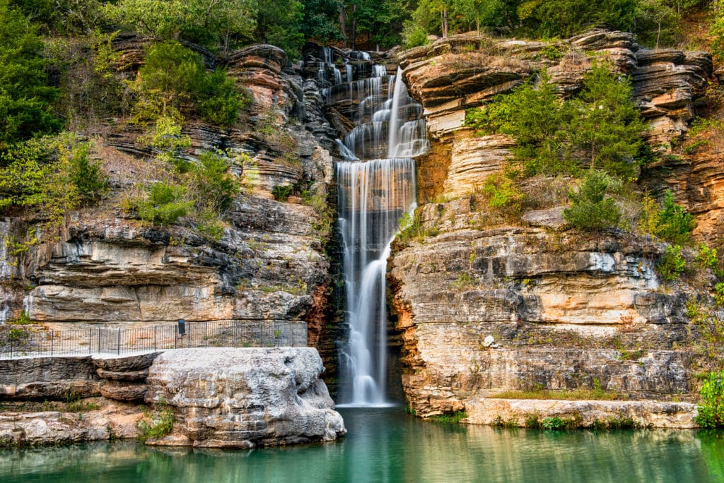 Beautiful waterfall falling down a cliff into emerald water at Dogwood Canyon In Branson, Missouri.