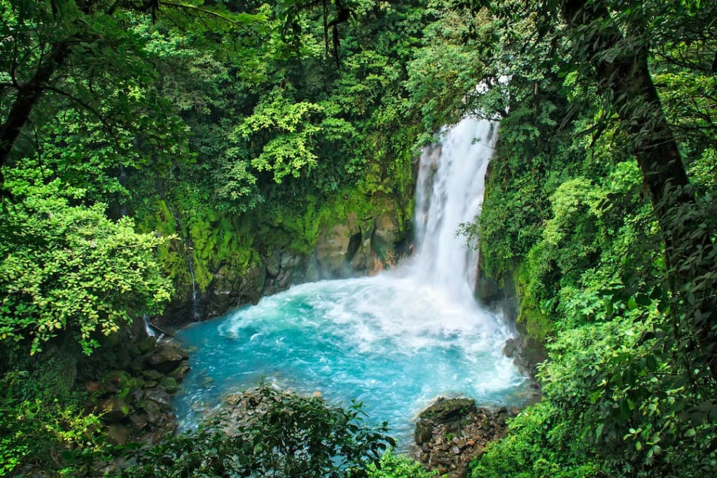 Powerful Bajos del Toro waterfall plunging into a turquoise pool, surrounded by steep cliffs covered in vibrant green vegetation in Costa Rica.