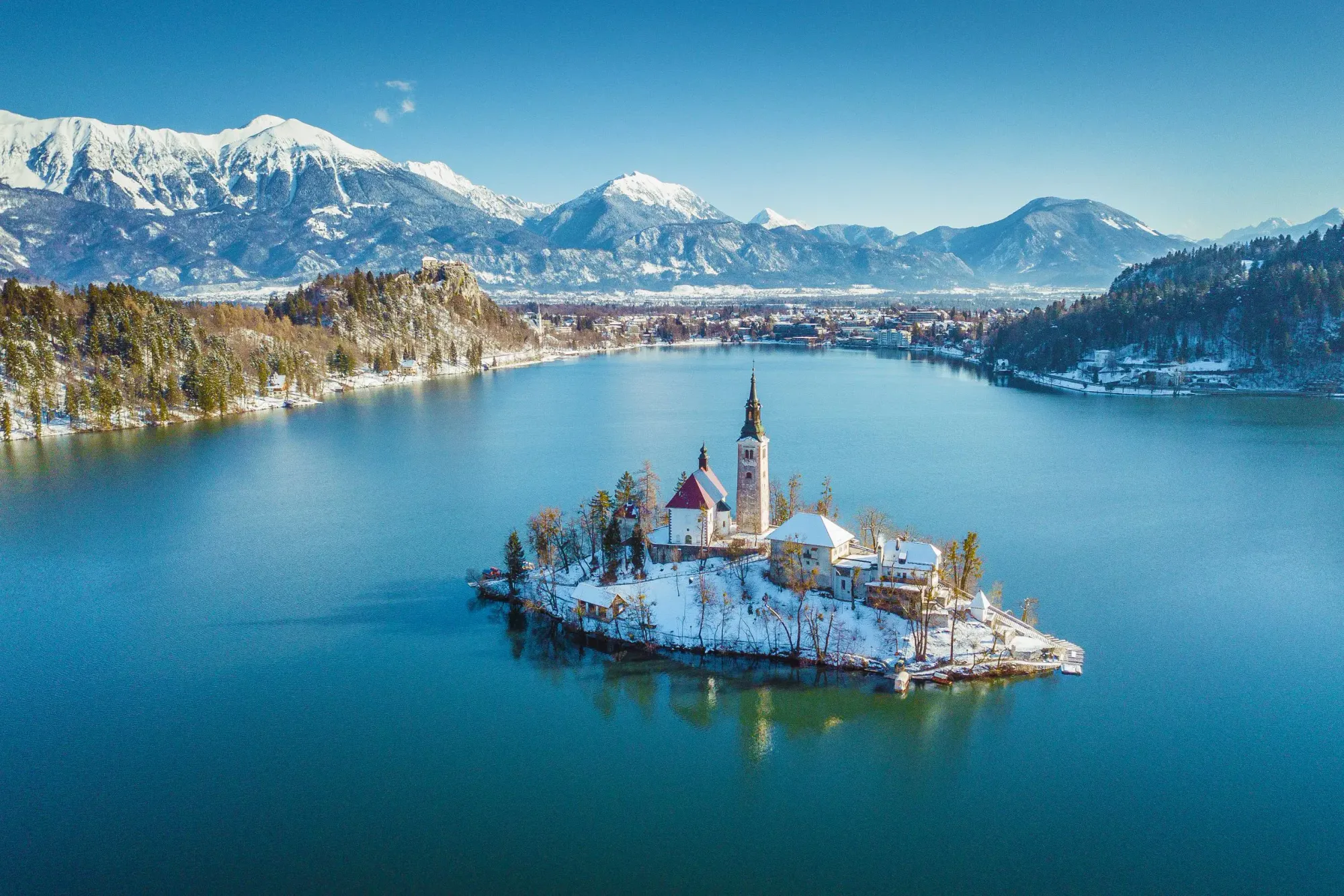 Snowy church island and alpine peaks reflect in the calm winter waters of Lake Bled.
