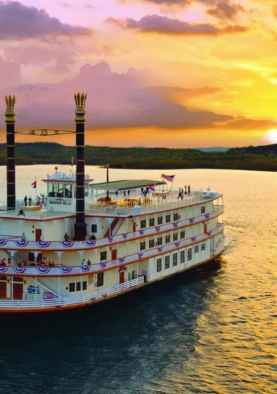 A 4 level boat on a lake at sunset in Branson Missouri with people onboard for a dinner and show on the lake. 