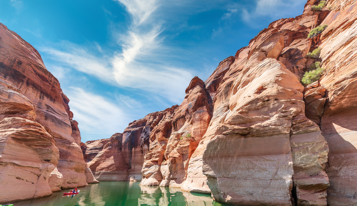Kayakers glide through the narrow red-rock walls of Antelope Canyon at Lake Powell on a bright, sunny day.