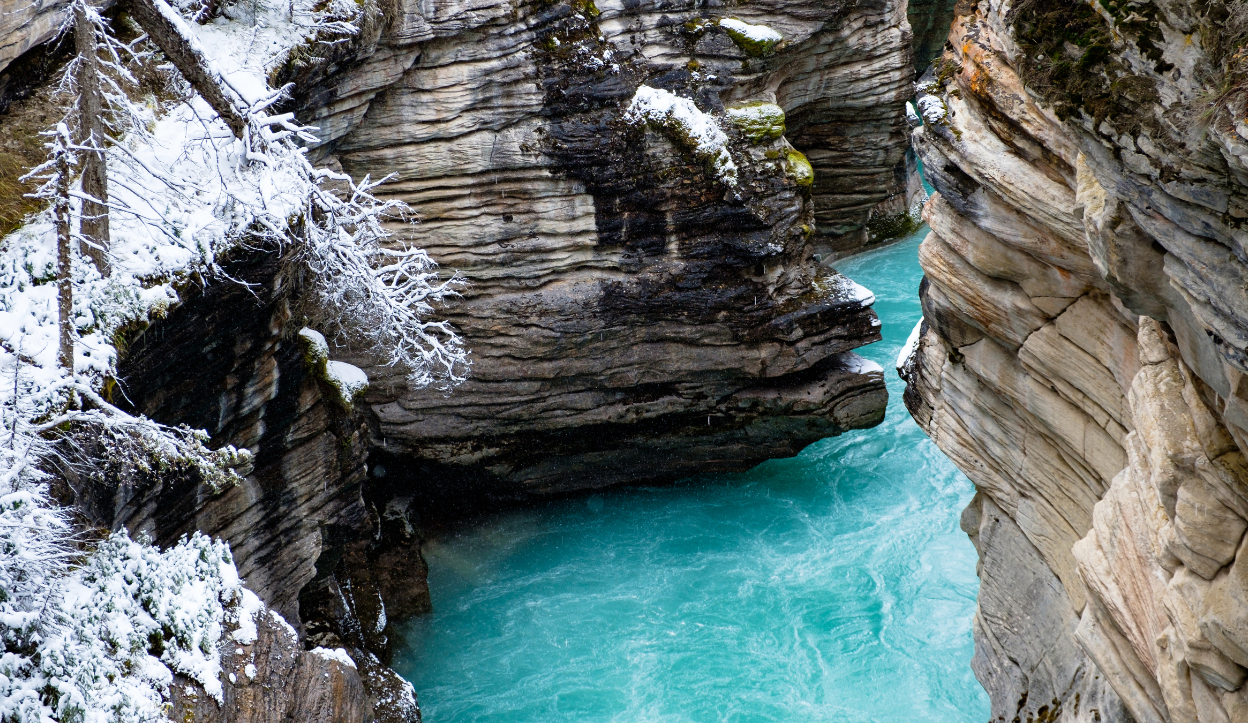 Turquoise river flowing through a narrow canyon with layered rock walls and snow-dusted trees in Jasper National Park, Canada.