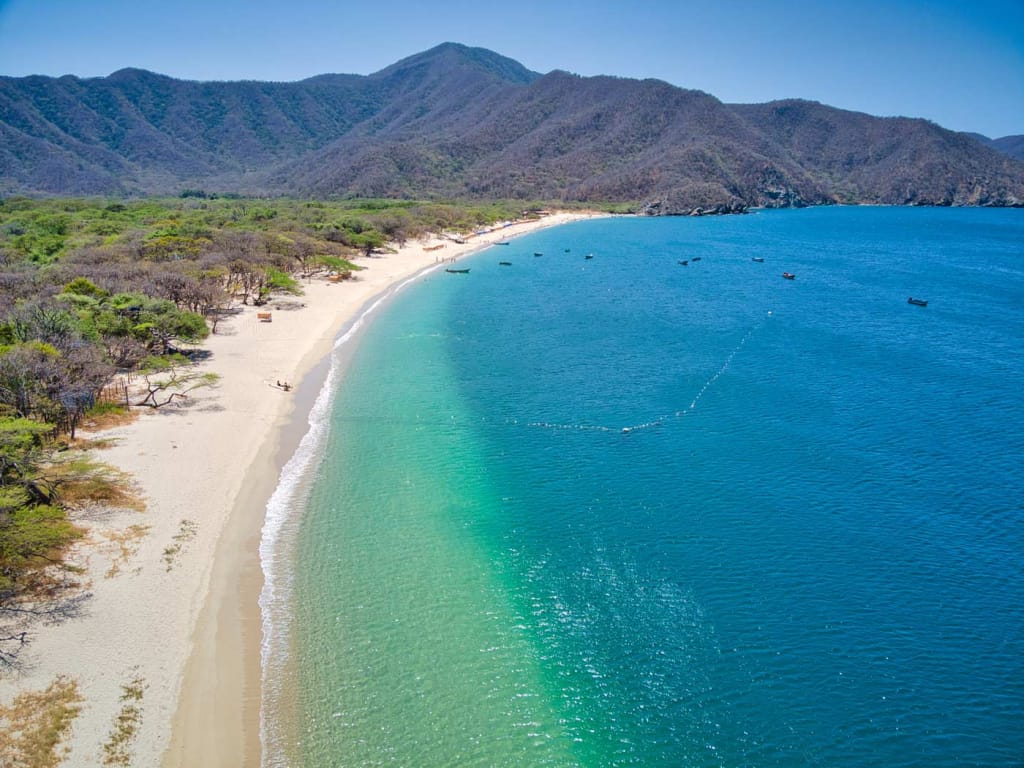 Bahía Concha in Tayrona National Park—wide bay with calm turquoise water and tree-covered mountains in the background.