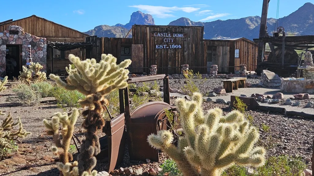 Cactus and old mining equipment in front of old outpost buildings at Castle Dome Mines Museum and Ghost Town in Yuma, Arizona.