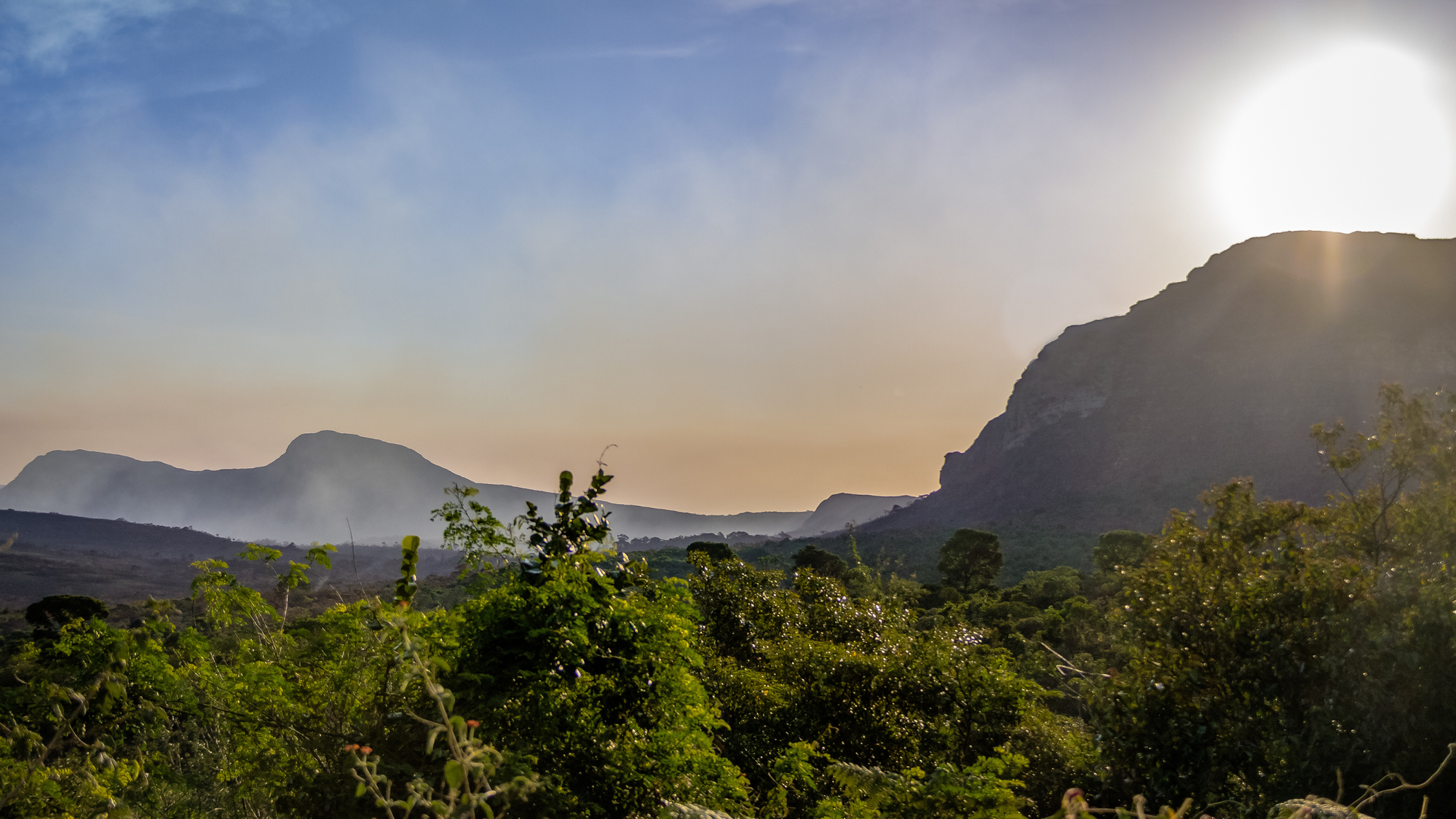 Sunrise over the lush green hills and rocky plateaus of Chapada Diamantina National Park in Brazil, with mist in the valleys and a bright sky.