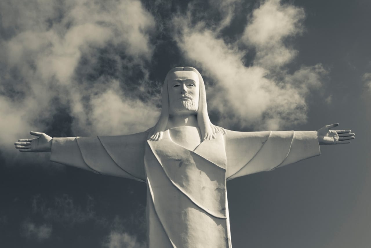  Front view of the Christ of the Ozarks statue in Eureka Springs, Arkansas, with outstretched arms against a cloudy sky in black and white.