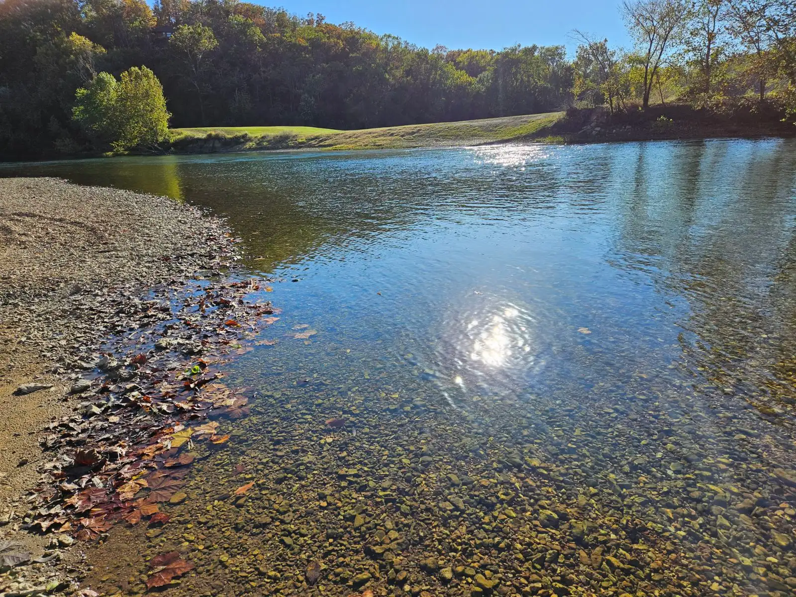 A gravel bar going out into the clear Current River in Van Buren, Missouri with the mid-day reflecting off a calm portion of the river.