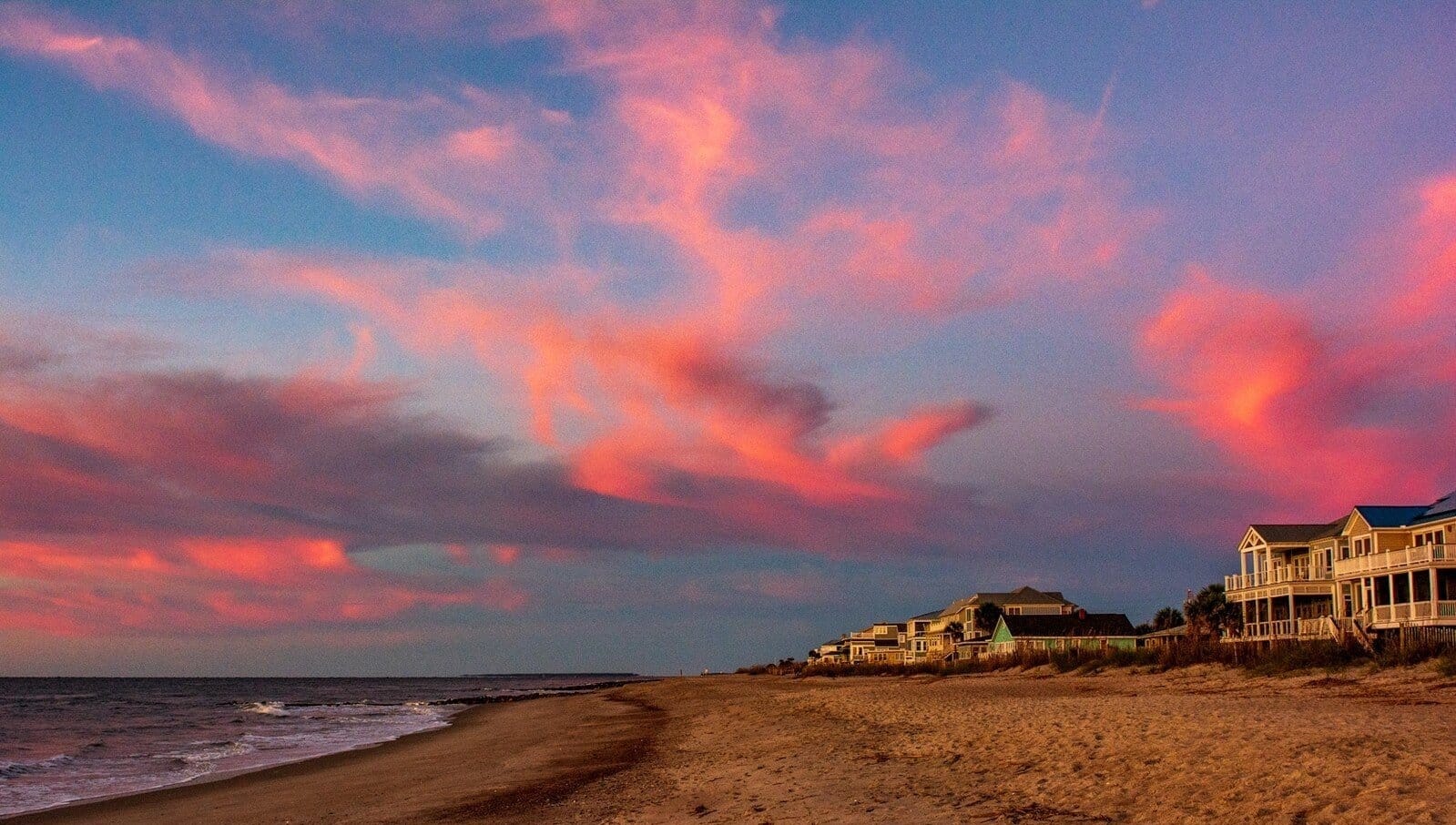 Coastal view of Edisto Beach on Edisto Island, South Carolina, with colorful sunset clouds, a quiet beach, and beachfront houses along the shoreline.