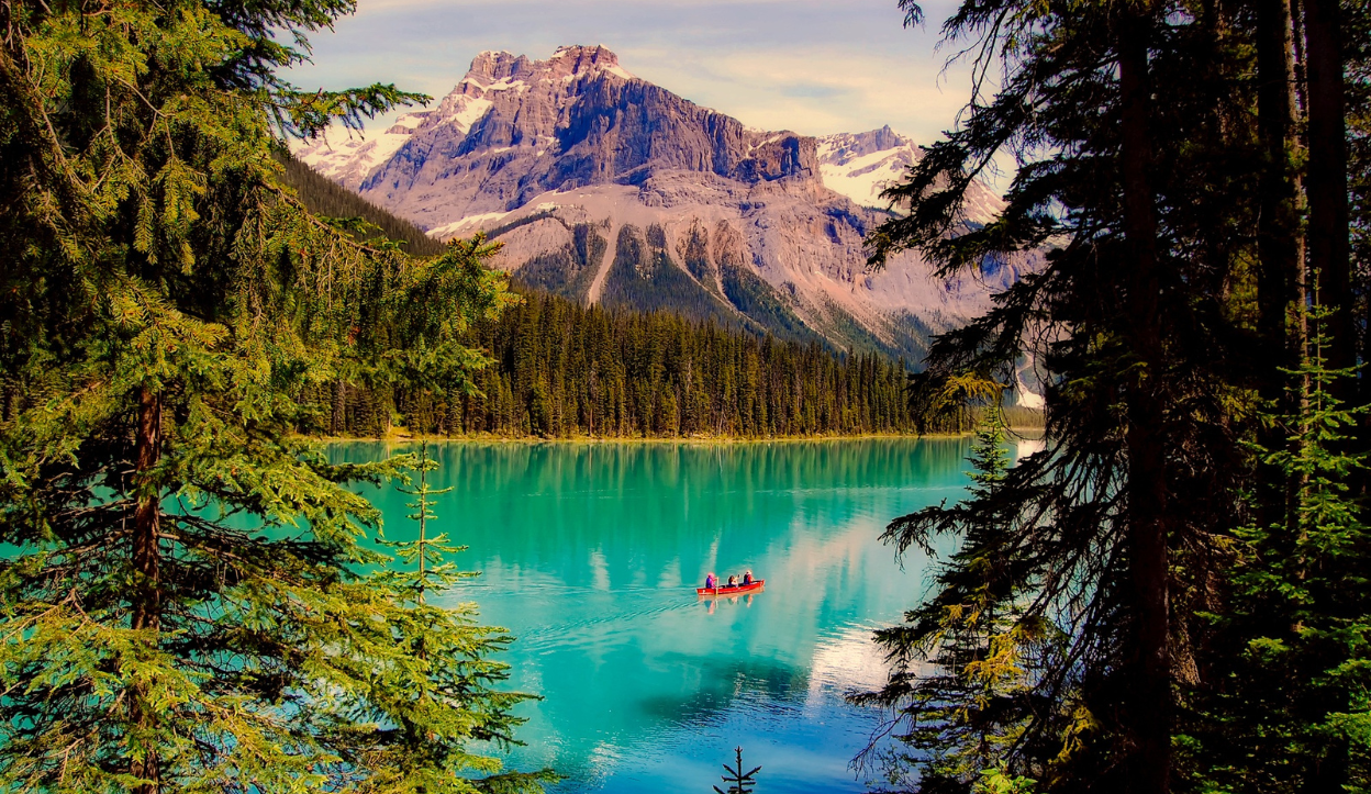 People canoeing on the striking turquoise waters of Emerald Lake, framed by evergreen trees and snow-capped peaks in Yoho National Park, Canada.