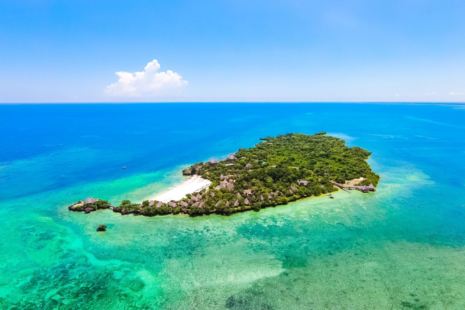 Aerial view of Funzi Island, Kenya, featuring lush green vegetation, traditional thatched-roof huts, and white sandy beaches surrounded by turquoise ocean waters.