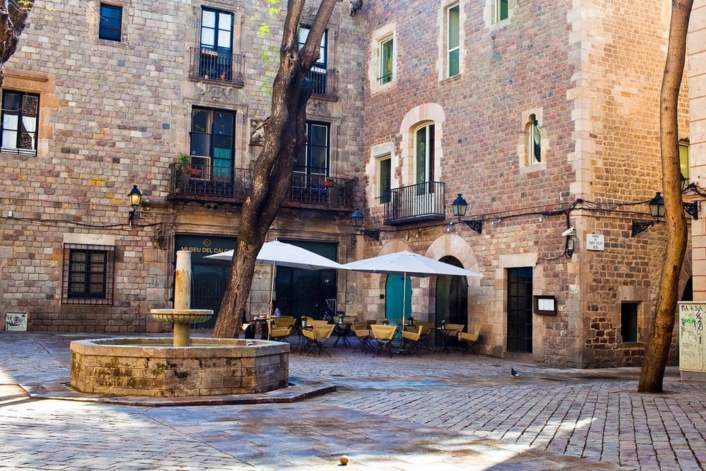 Charming outdoor seating area in a stone-paved square near Hotel Neri Relais & Châteaux in Barcelona’s Gothic Quarter, with a central fountain and historic brick buildings.