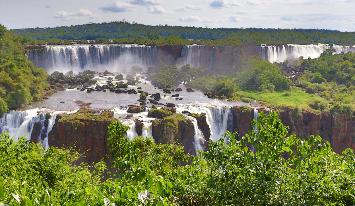 Multiple powerful waterfalls cascade over cliffs surrounded by lush green rainforest in Iguazú National Park, Argentina, creating mist and dramatic scenery.