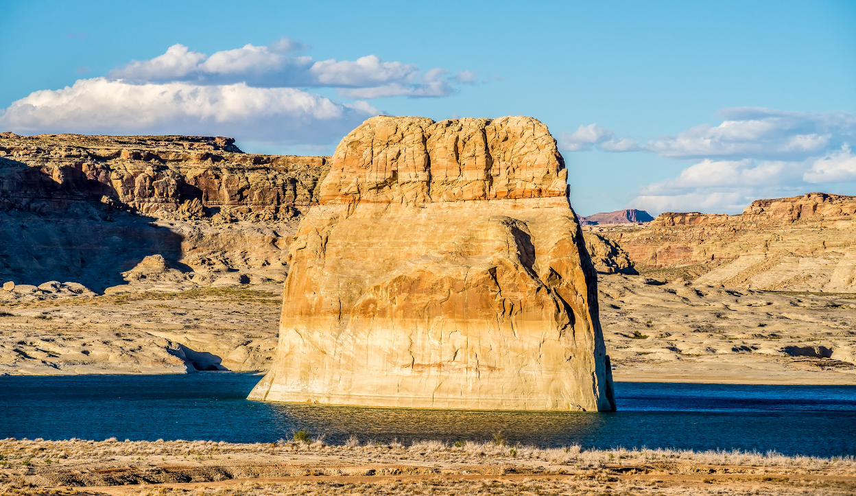 A large lone Rock rises from the blue waters of Lake Powell.