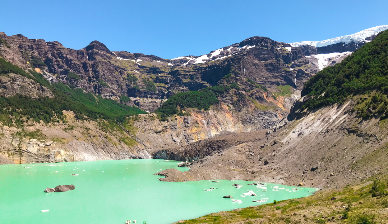 Glacial lake with turquoise waters surrounded by rocky cliffs and patches of forest in Nahuel Huapi National Park, Argentina, with small icebergs floating on the surface.