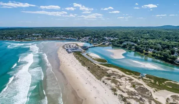 Scenic aerial image of Ogunquit Beach in Maine showing waves crashing on the sandy beach, tidal rivers meeting the ocean, and a populated coastal town in the background.