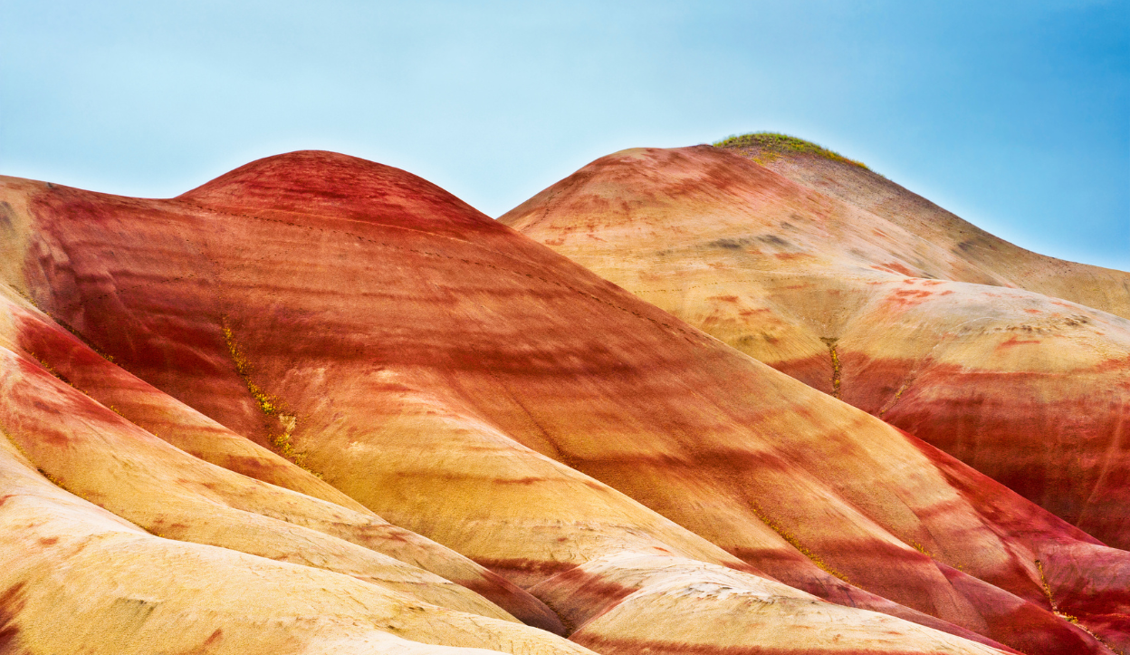 Vividly colored rolling hills in shades of red, orange, and yellow at the Painted Hills, part of the John Day Fossil Beds National Monument in Oregon, under a clear blue sky.