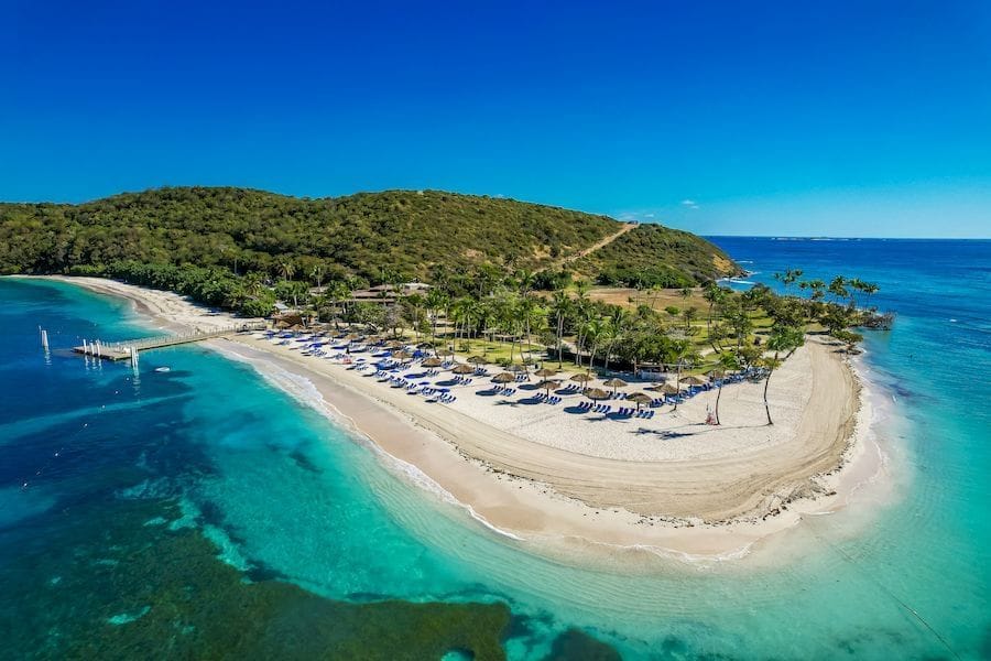 Palomino Beach in northern Colombia—golden sand coastline framed by green hills and bright blue Caribbean water.