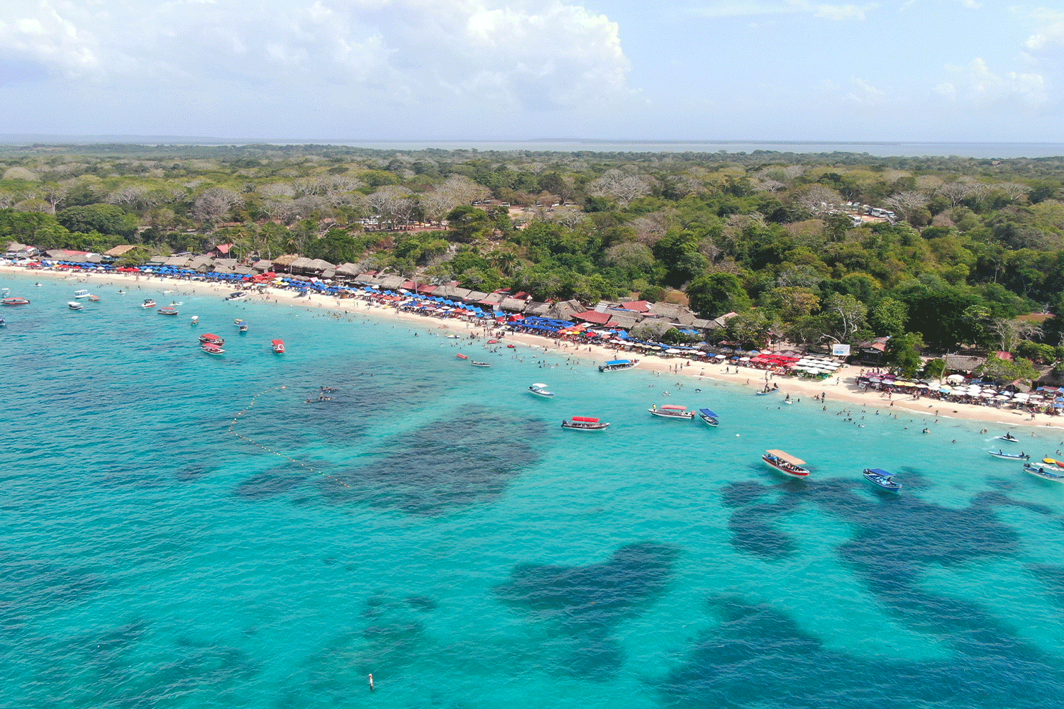 Playa Blanca in Barú, CoAerial view of Playa Blanca near Cartagena, Colombia—busy beach with colorful umbrellas, thatched huts, and turquoise water filled with small boats.