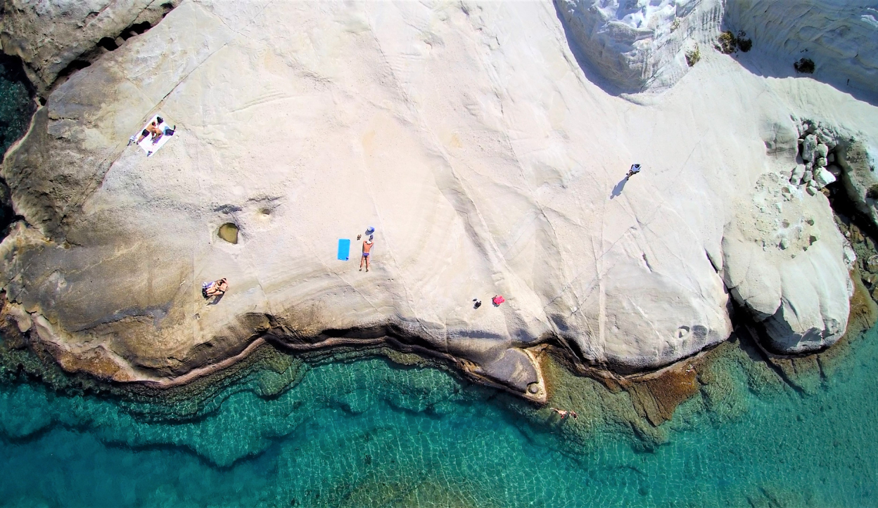 Crystal-clear blue waters at Sarakiniko Beach in Milos, Greece, surrounded by smooth, white volcanic rock formations resembling a lunar landscape.