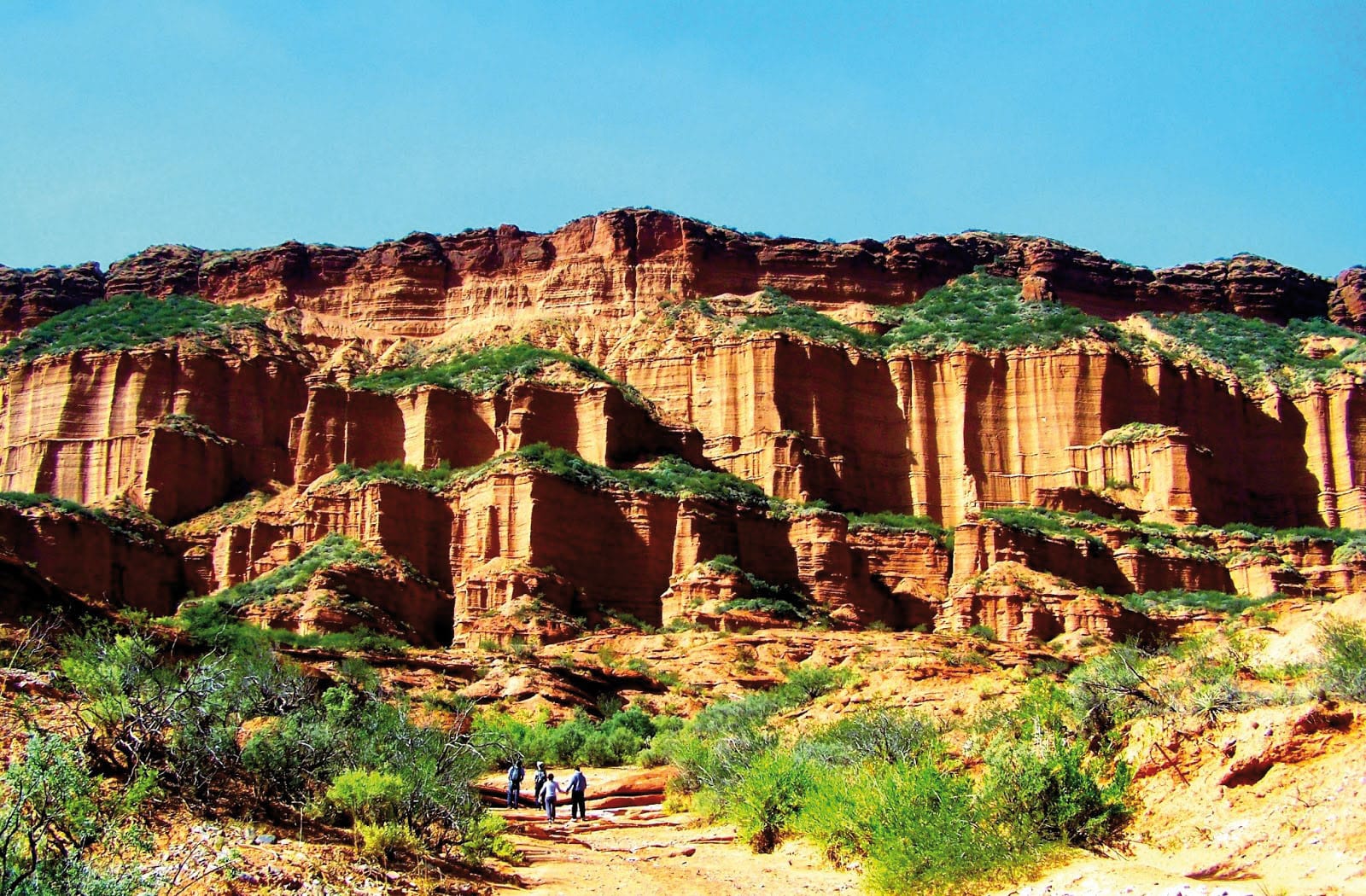 People walking in a desert with red rock mountains in the background at Sierra de las Quijadas National Park.