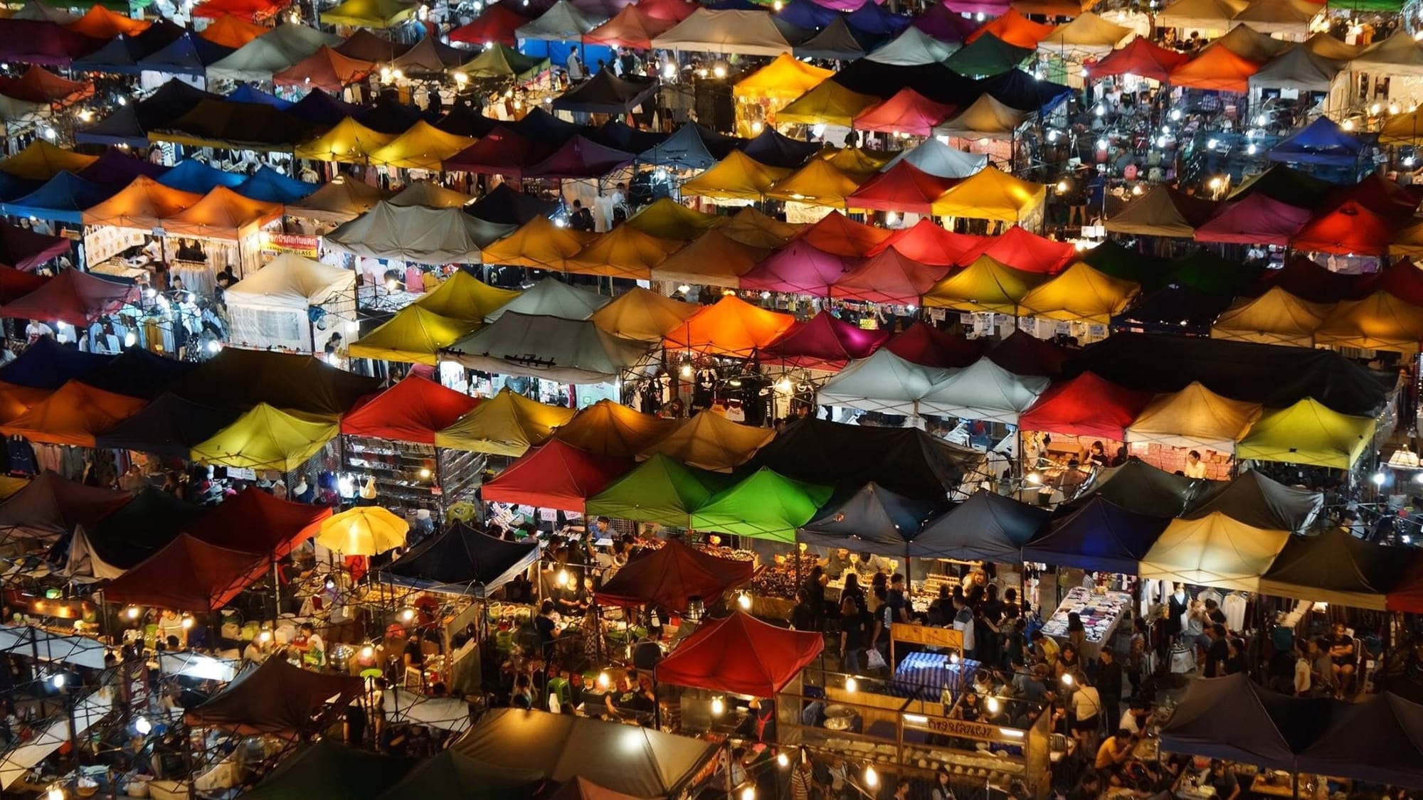 Ariel view of colorful tents at the Tha Din Daeng Market in Bangkok at night.