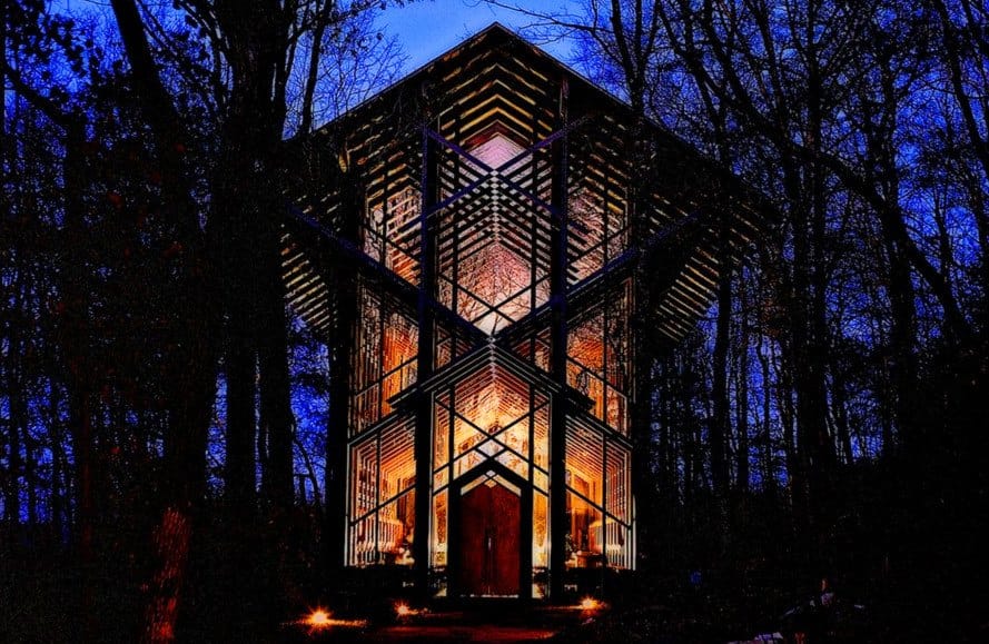 Illuminated Thorncrown Chapel at night in Eureka Springs, Arkansas, surrounded by trees and glowing with interior light through its glass walls.