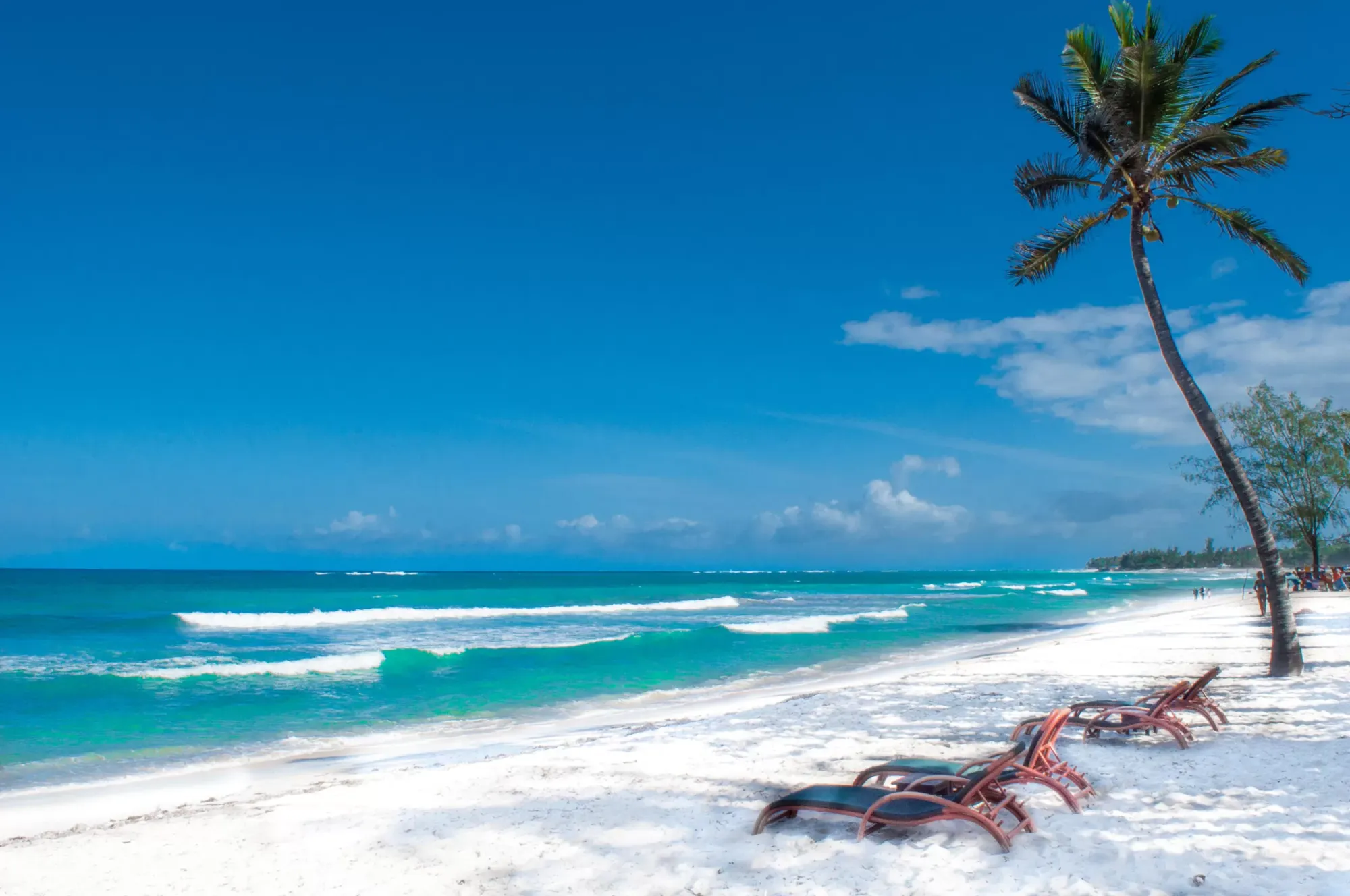 Aerial view of Tiwi Beach in Kenya, showing white sandy shores, shallow turquoise waters, palm-lined coast, and a kitesurfer gliding across the ocean.