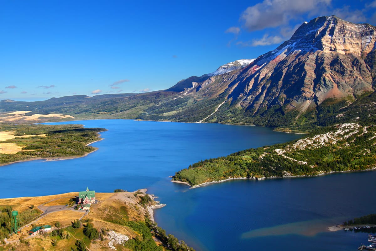 Panoramic view of a deep blue lake surrounded by forested hills and rugged mountains in Waterton Lakes National Park, Canada.