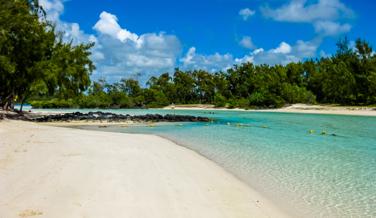 Scenic view of Île aux Cerfs Beach in Mauritius with white sand, turquoise water, and lush green trees under a bright blue sky.