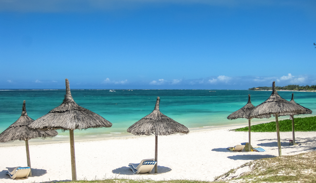 Belle Mare Beach in Mauritius featuring thatched umbrellas and sun loungers on soft white sand beside the calm, clear blue ocean.