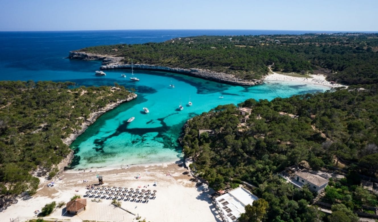 Aerial view of Sa Calobra Beach in Mallorca, Spain, showing a deep turquoise bay nestled between rugged cliffs and forested hills.