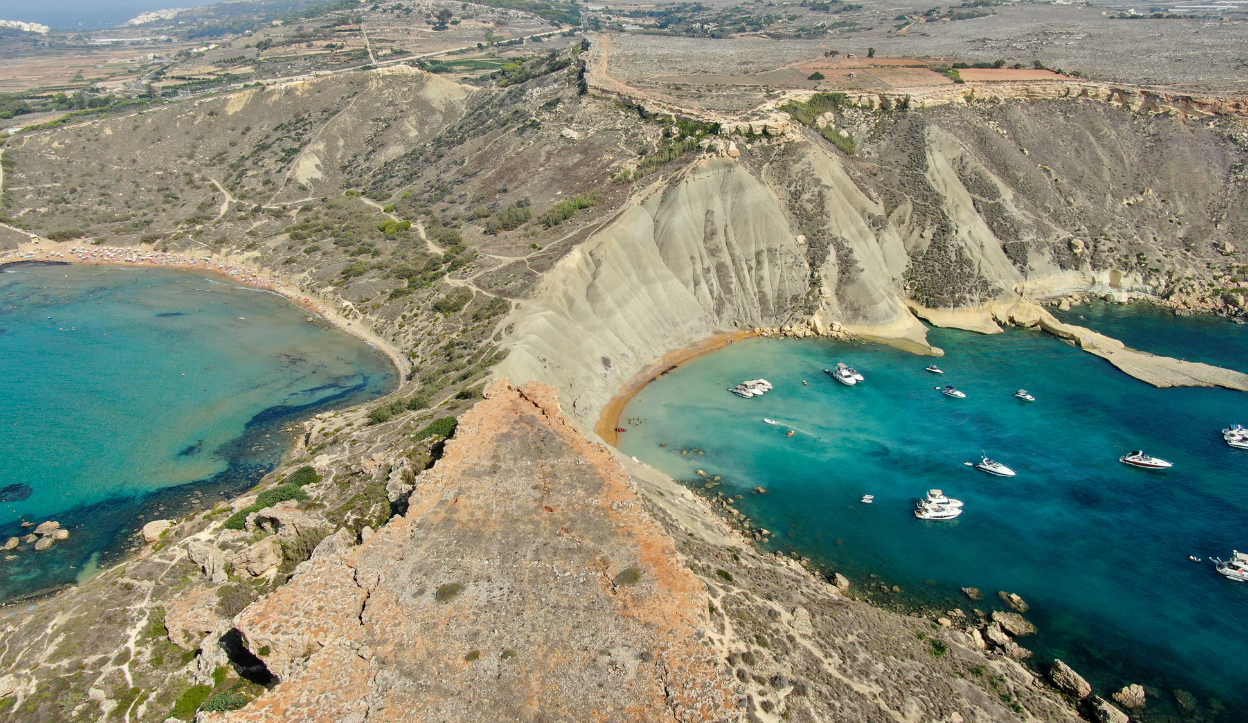 Aerial view of Għajn Tuffieħa Bay in Malta, featuring twin sandy beaches separated by dramatic cliffs, with boats anchored in the bay.