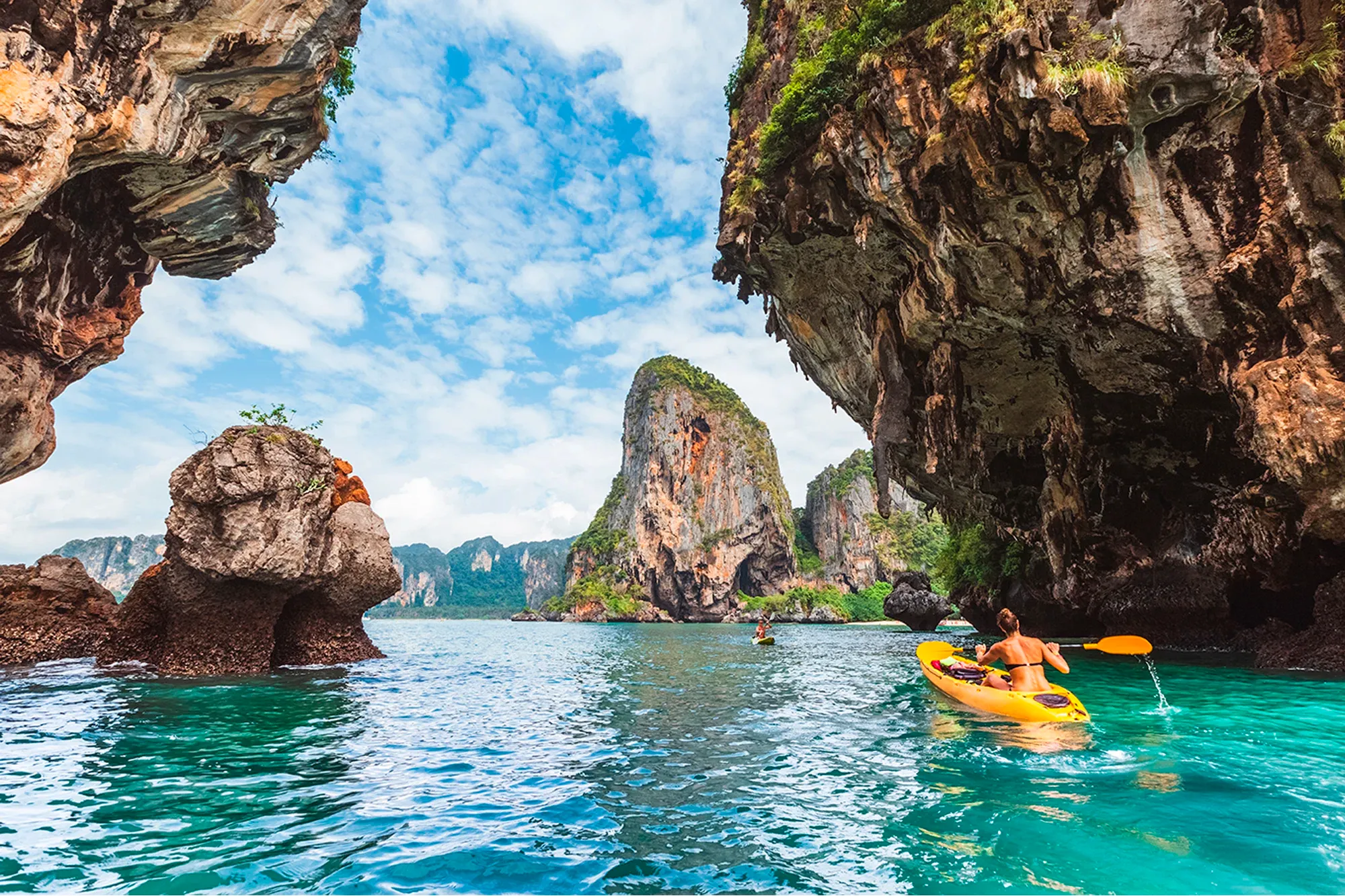 Woman kayaking through limestone cliffs in Krabi, Thailand.