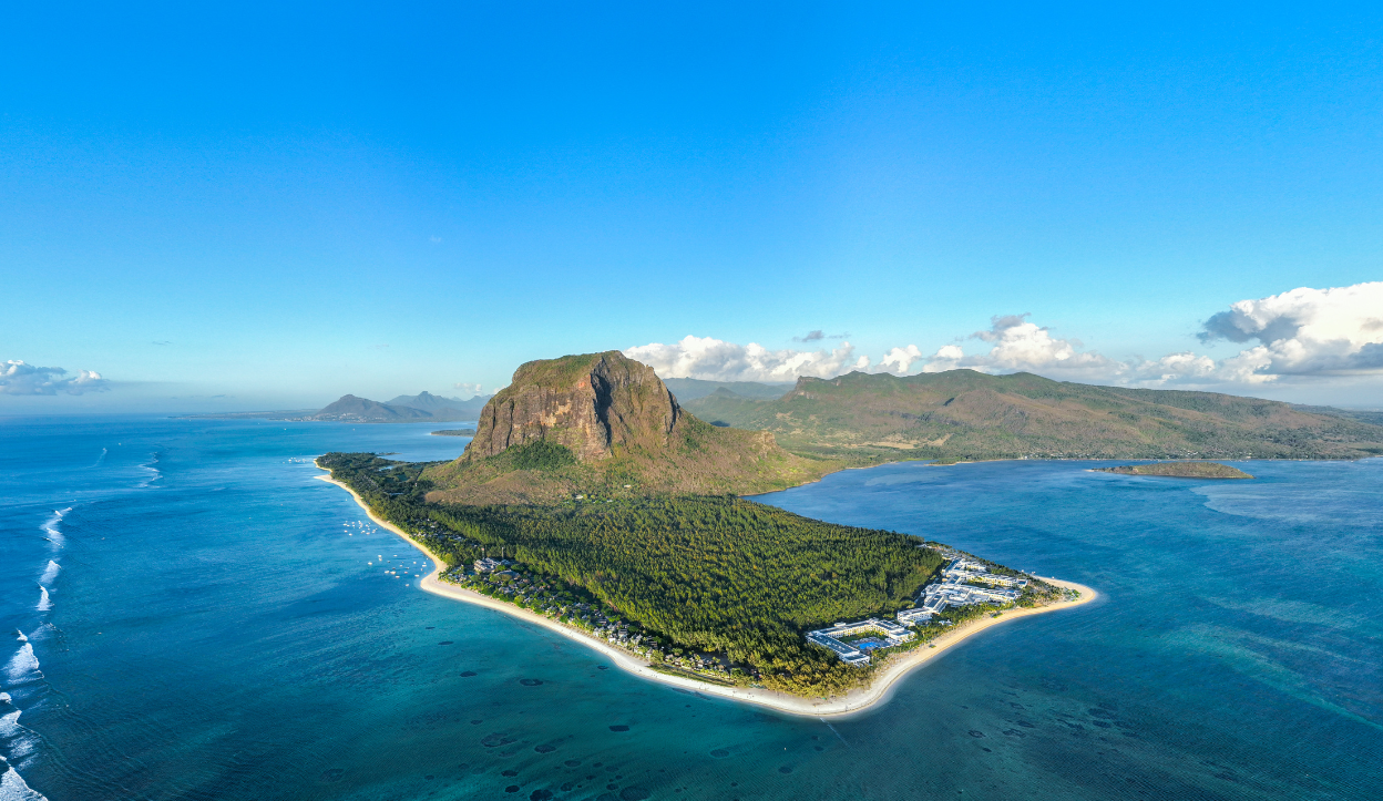 Aerial view of Le Morne Beach in Mauritius with a dramatic mountain backdrop, dense forest, and surrounding turquoise waters.