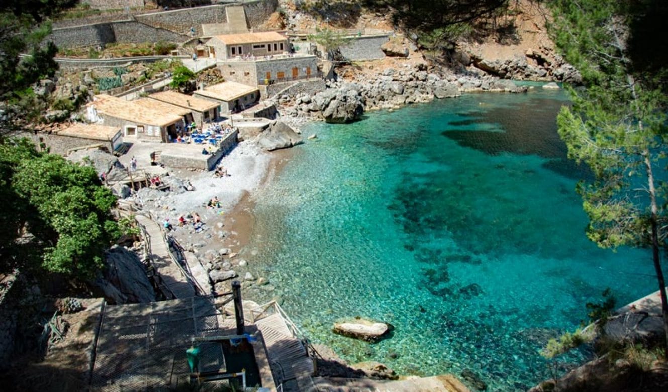 Aerial view of Sa Calobra Beach in Mallorca, Spain, showing a deep turquoise bay nestled between rugged cliffs and forested hills.