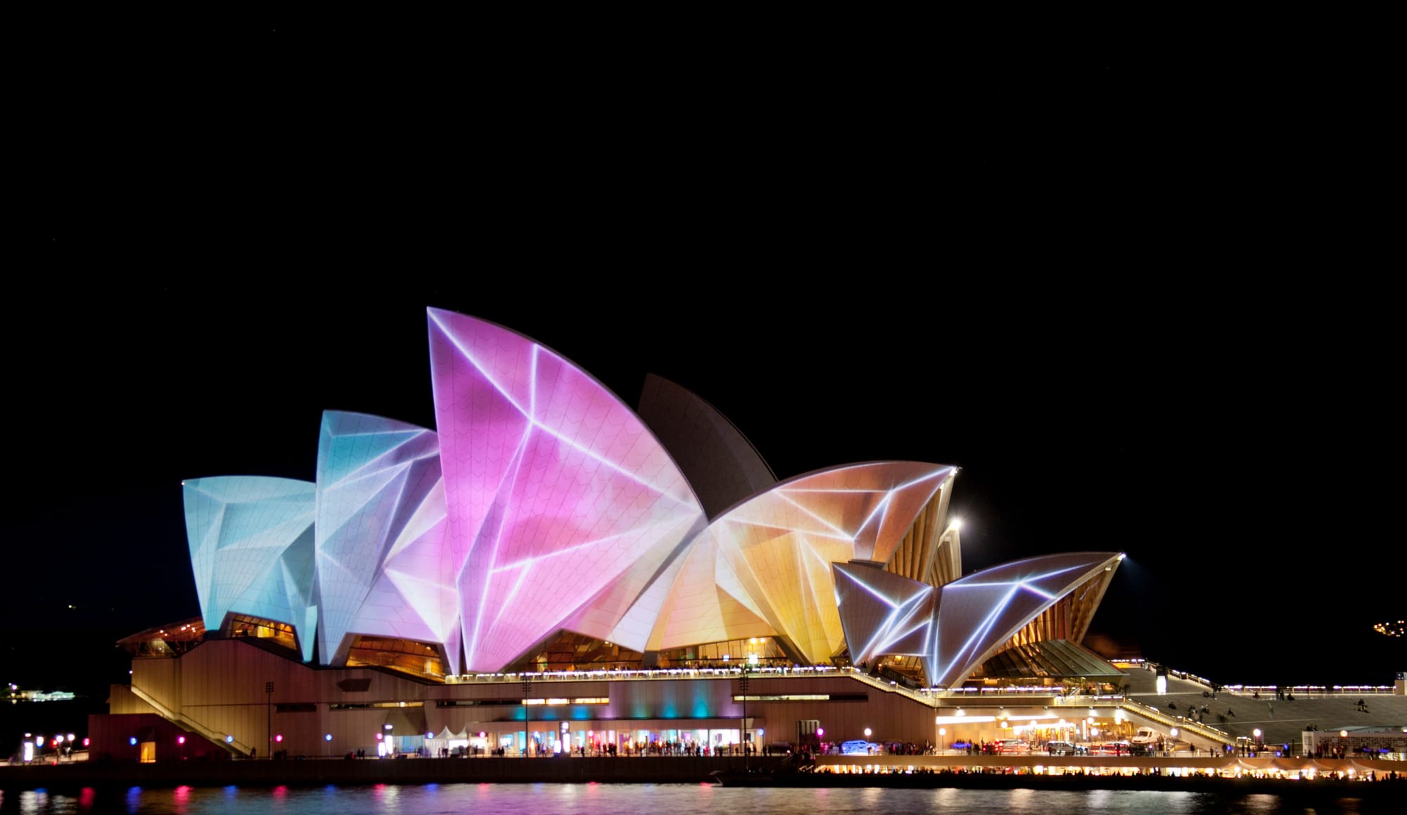 Sydney Opera House Lit Up At Night With Various Colors.