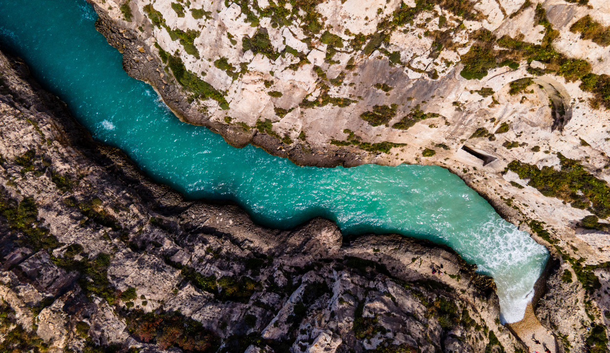 Aerial view of Wied il-Għasri in Gozo, Malta, featuring a narrow turquoise inlet winding between steep limestone cliffs with patches of greenery.