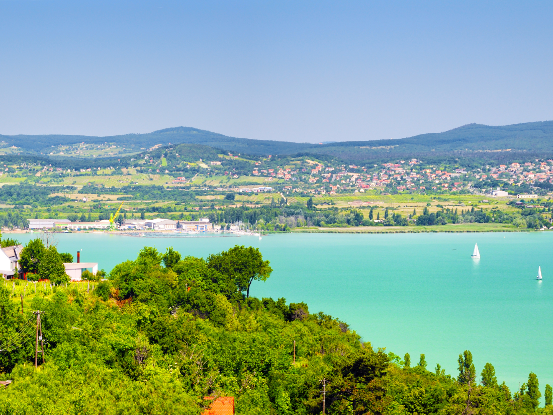 Lake Balaton, Hungary is a beautiful blue colored lake where sailboats can be seen enjoying a sunny summer day.