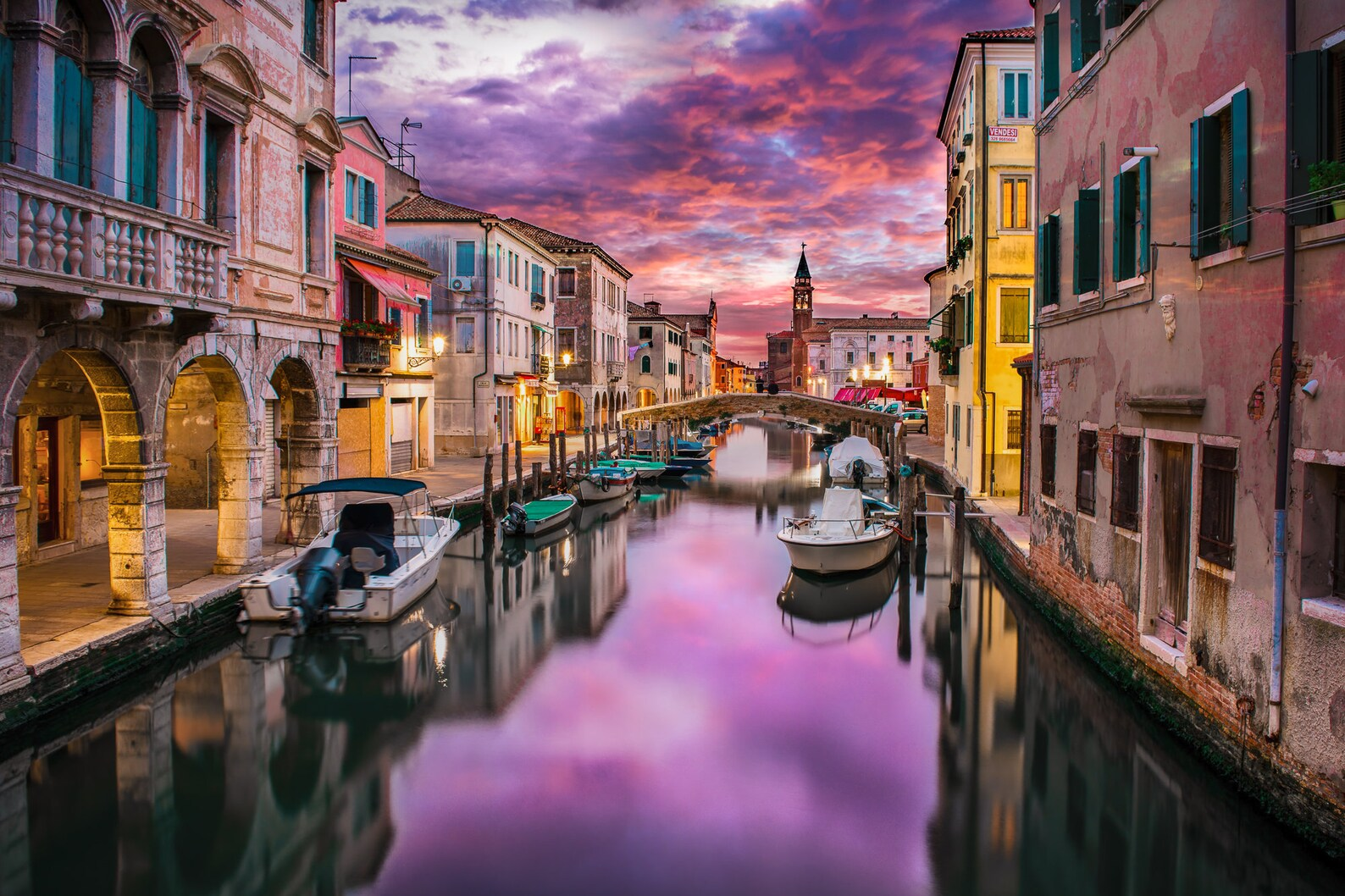 Venice canal at sunset with boats parked along Italian style homes. 