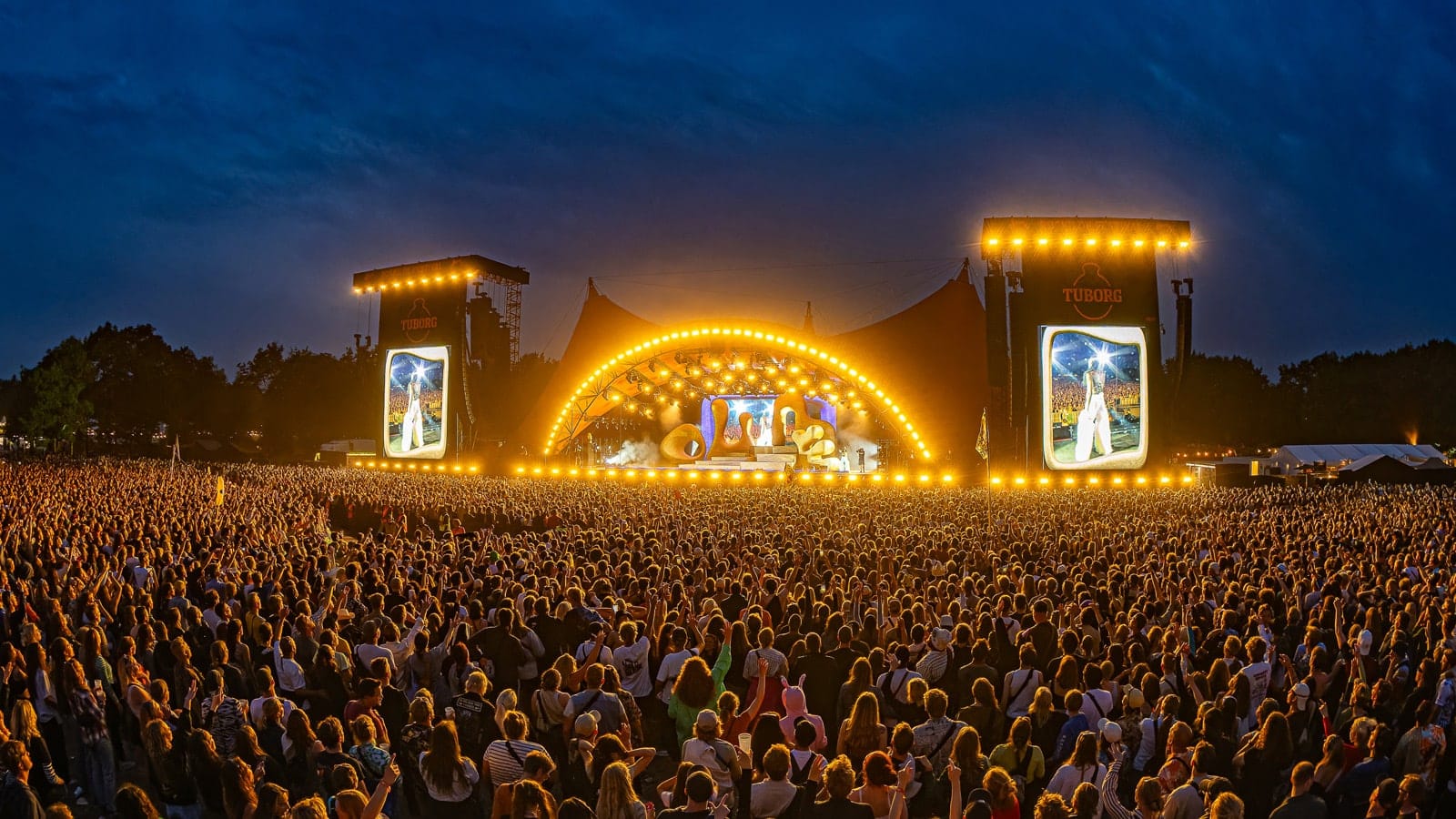 Lots of people watching a concert at night at the annual Roskilde Festival.