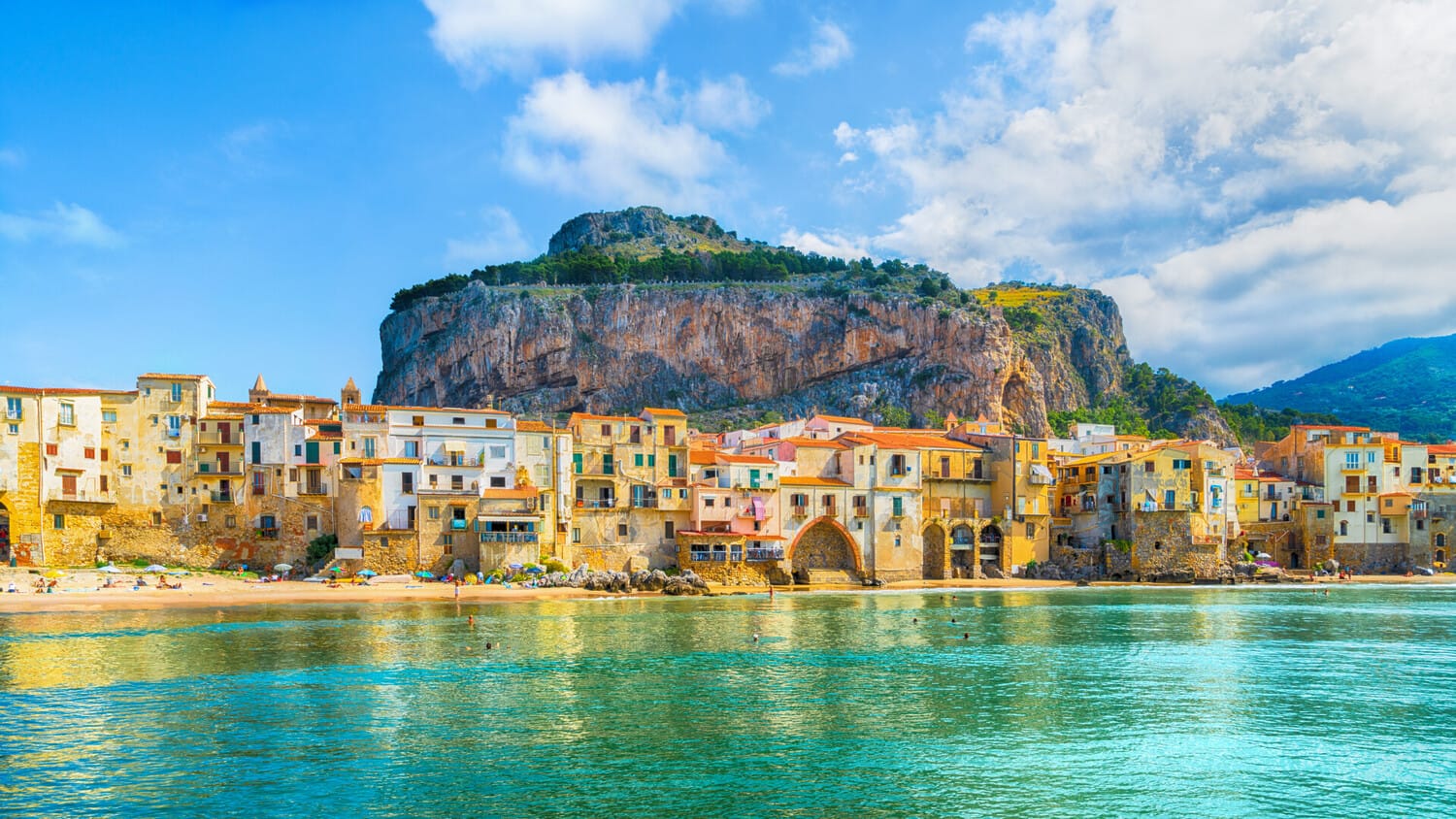 Cefalù seaside village in beach with mountain in background.