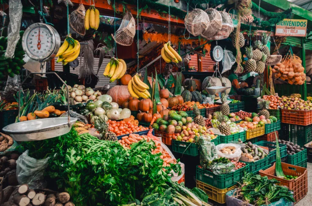Fruit market in Bogota showing a vendors fruit stand with Bananas hanging, and many other fruits on colorful display.