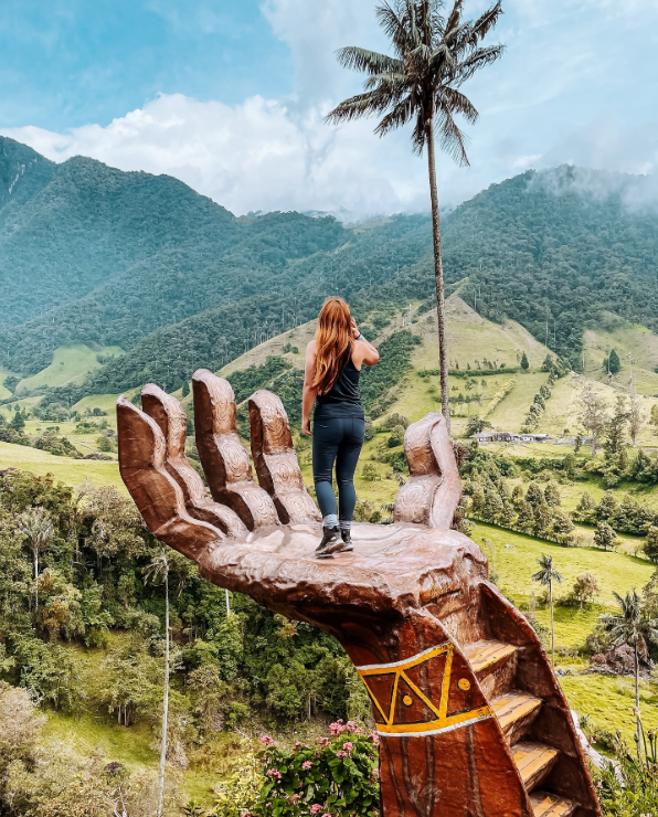 A woman standing on a giant hand in COCORA VALLEY, Colombia.