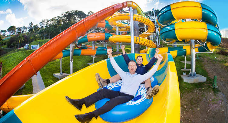 A giant yellow and blue striped innertube slide with two men riding it at The Big Banana Fun Park — Coffs Harbour, Australia