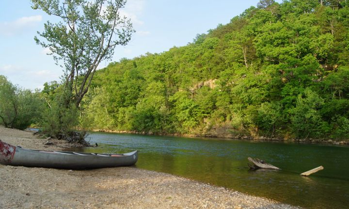 Current River in Van Buren, Mo with a canoe parked on the gravel bar, and other side of the river is a cliff with trees. 