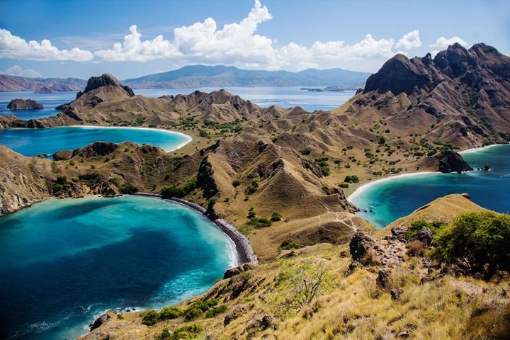 Ariel view of Komodo National Park showing 3 beaches with beautiful clear blue waters surrounded by mountains.