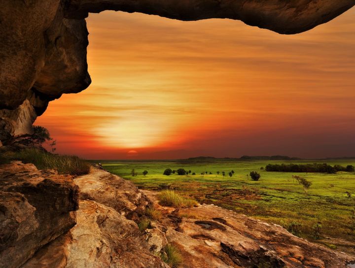 View of the Australian plains at sunset with a red rock cliff beside green fields.